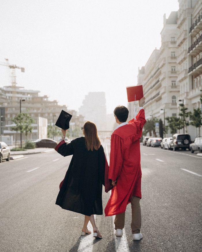 A joyful couple of graduates in gowns and caps celebrating in a city street.