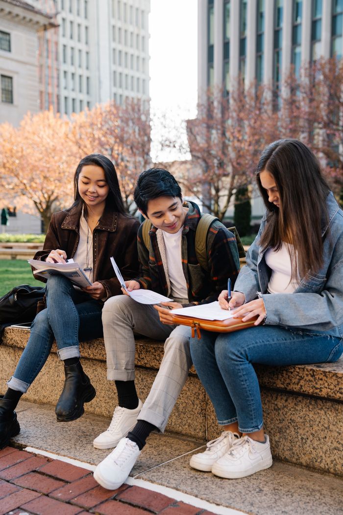 A group of young students studying together on a sunny day in an urban setting.